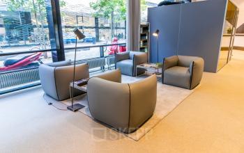 Moderne gemeubileerde lounge met grijze fauteuils en staande lampen bij Weena 290, ideaal voor kantoorruimte huren in Rotterdam Centraal Station.