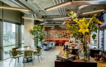 Moderne kantoorruimte in Hofplein 19, Rotterdam met stijlvolle inrichting en grote ramen die veel natuurlijk licht binnenlaten. Personen zijn bezig met overleg aan tafels.