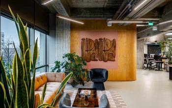 Stijlvolle kantoorruimte op Hofplein 19, Rotterdam, met moderne meubels, houten accenten en veel groen. Gedeeltelijk zicht op werkplekken met bureaus. Perfect voor het huren van een inspirerende werkomgeving.