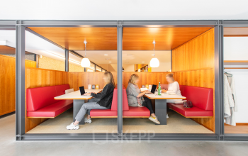 Zakelijke bespreking in moderne kantoorruimte met rode banken op Hofplein 20, Rotterdam Centraal Station. Vergadering in een professioneel ingerichte omgeving met warme houten accenten.