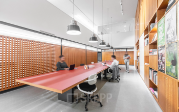 Moderne kantoorruimte met houten wanden en lange roze tafel, geschikt voor werken of vergaderen. Personen werken aan laptops. Gelegen in Rotterdam Centraal Station, Hofplein 20.