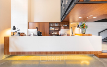 Moderne receptie in kantoorpand op Hofplein 20, Rotterdam Centraal Station. Twee mensen werken achter balie met computers en bloemen. Kantoorruimte huren met professionele uitstraling.