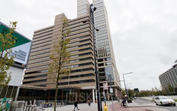 Kantoorpand aan Weena 750 in Rotterdam Centraal Station. Moderne gevel met ramen en steen, fietser op de voorgrond.