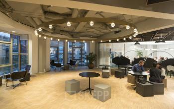 Kantoorruimte huren op Stationsplein 45, Rotterdam Centraal Station, modern ingerichte ruimte met zitgelegenheid en glazen wanden. Personen zijn bezig met zakelijke activiteiten.