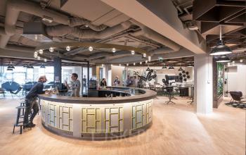 Ruime, moderne kantoorruimte huren op Stationsplein 45, in Rotterdam Centraal Station. Gezellige sfeer met werknemers in overleg rondom een unieke ronde bar, met comfortabele zitplekken en eigentijdse inrichting.