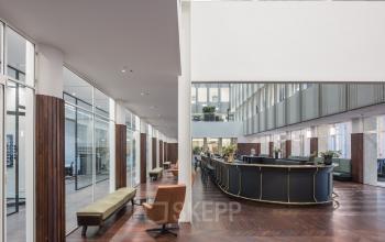 Interieur van kantoorpand op Blaak 34, Rotterdam Centrum met moderne werkruimtes en een grote receptiebalie. Verschillende mensen zijn bezig met zakelijke activiteiten.