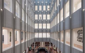 Ruime kantoorpand aan Blaak 34 in Rotterdam Centrum met meerdere verdiepingen en open werkruimtes. Grote ramen zorgen voor veel natuurlijk licht. Twee personen zijn bezig met zakelijke activiteiten.