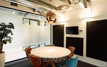Vergaderruimte in kantoor op Westblaak 90, Rotterdam Centrum. Moderne inrichting met ronde tafel, kleurrijke stoelen en een muur-TV. Industriële details en planten zorgen voor een professionele sfeer.