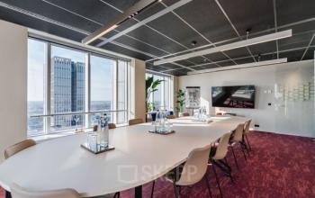 Moderne vergaderruimte met lange ovale tafel en comfortabele stoelen, grote ramen geven uitzicht op Rotterdam. Ideale kantoorruimte huren op Weena 690 voor effectieve meetings.