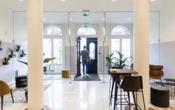 Lichte entree van kantoorpand op Westplein 12 in Rotterdam Centrum, met een persoon die de deur opent, diverse planten en zitgelegenheden. Ideaal voor kantoorruimte huren.