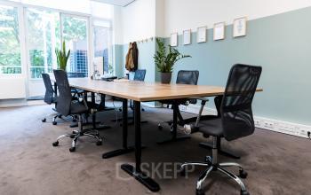 Kantoorruimte huren in Westplein 12, Rotterdam Centrum. Vergaderruimte met moderne stoelen, houten tafel, planten en muurdecoratie. Veel natuurlijk licht door grote ramen.