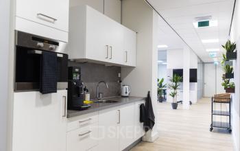 Kantoorpand op Westplein 12, Rotterdam Centrum, met moderne pantry inclusief koffiemachine, oven en kraan, met zicht op gang en werkplekken.