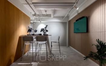 Vergaderruimte in kantoorpand op Vasteland 42-110, Rotterdam Centrum met hoge stoelen, tafel, groen plantje, scherm aan de muur en verlichting aan het plafond.