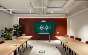 Moderne vergaderruimte met lange houten tafels, rode stoelen en een groot scherm, ideaal voor kantoorruimte huren in Rotterdam Centrum.