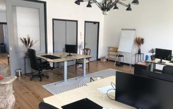 Kantoorpand Schiekade 105, Rotterdam Centrum. Moderne kantoorruimte met houten vloer, bureaus, stoelen en computers. Personen zijn aanwezig en bezig met werkactiviteiten. Flip-over en planten in de ruimte.