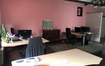 Kantoor in Rotterdam Centrum op Schiekade 105 met bureaus, stoelen en computers. Diverse werkplekken en planten in de ruimte, gemoderniseerd met een houten dressoir.