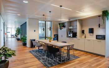 Moderne kantoorruimte op Weena 788 in Rotterdam Centrum met een stijlvolle vergadertafel, comfortabele stoelen en een kitchenette met apparaten. Gezellig verlicht en ingericht voor huur, ideaal voor zakelijke bijeenkomsten.