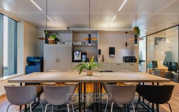 Functionele kantoorruimte te huur met een lange tafel en verschillende stoelen, voorzien van moderne apparatuur en natuurlijke decoratie, ideaal gelegen op Weena 788 in Rotterdam Centrum.