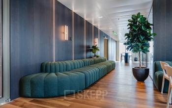 Stijlvolle en moderne kantoorruimte huren op Weena 788, Rotterdam Centrum, met houten vloeren, chique zitbank en planten, ideaal voor een zakelijke ambiance.