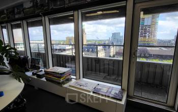 Kantoorpand op Aert van Nesstraat 45 in Rotterdam Centrum met grote ramen en uitzicht op de stad, met boeken op een tafeltje.