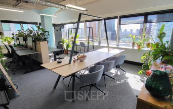 Kantoorruimte huren op Aert van Nesstraat 45 in Rotterdam Centrum met werkplekken voorzien van bureaus, stoelen en planten, en uitzicht op de stad door grote ramen.