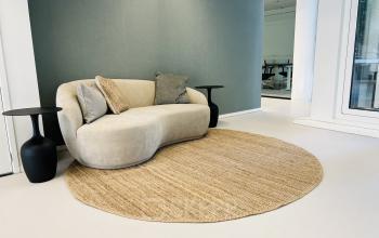 Lichte, moderne entree met een beige bank en ronde juten vloerkleed in kantoorpand op Kruisplein 480, ideaal voor kantoorruimte huren in Rotterdam Centrum.