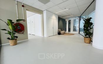 Ontvangstruimte van kantoorpand op Kruisplein 480, Rotterdam Centrum, met strakke witte muren, moderne meubels, grote planten en veel licht door glazen wanden. Ideale locatie voor kantoorruimte huren.