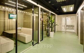 Moderne kantoorruimte huren aan Weena 335 in Rotterdam Centrum, met glazen vergaderhokken en groene vloer, biedt een frisse werkomgeving.