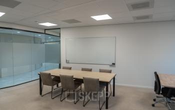 Kantoorruimte huren met vergadertafel en stoelen op Weena 335, Rotterdam Centrum. Glaswanden scheiden de ruimte, wat een open en lichte sfeer creëert.