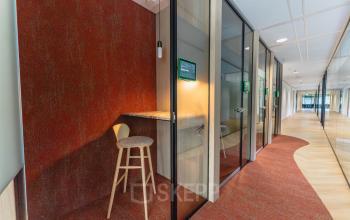 Moderne kantoorruimte op Blaak 555 in Rotterdam Centrum met glazen wanden en een hoge kruk. Ideaal om te huren voor zakelijke bijeenkomsten en dagelijks werk. Heldere, gestroomlijnde inrichting voor een professionele uitstraling.