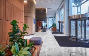 Moderne ontvangstruimte van kantoorpand Blaak 555 in Rotterdam Centrum met marmeren vloer, planten en meubels. Mensen voeren zakelijke gesprekken bij de balie. Ideaal voor kantoorruimte huren.