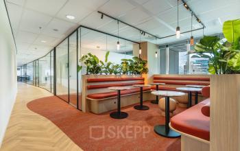 Modern ingerichte kantoorruimte op Blaak 555, Rotterdam Centrum, met glazen wanden, rode stoelen en groene planten voor een frisse uitstraling. Ideaal voor het huren van kantoren in een centraal gelegen kantoorpand.