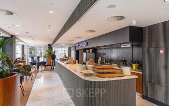Ruime, moderne kantine in het kantoorpand op Blaak 555, Rotterdam Centrum, met stijlvol interieur en eetgelegenheid. Mensen bereiden zich voor of genieten van een pauze.