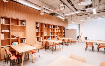 Moderne kantoorruimte in Rotterdam Centrum met houten tafels en stoelen, geschikt voor verhuur. De ruimte heeft een open indeling met boekenplanken tegen de muur, ideaal voor creatieve werkplekken.