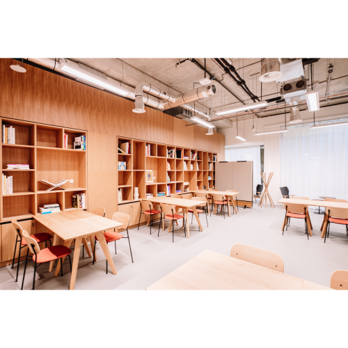 Moderne kantoorruimte in Rotterdam Centrum met houten tafels en stoelen, geschikt voor verhuur. De ruimte heeft een open indeling met boekenplanken tegen de muur, ideaal voor creatieve werkplekken.