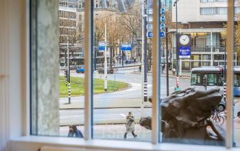 Uitzicht vanaf Weena 87 in Rotterdam Centrum. Grote ramen bieden zicht op het drukke stadsleven met voorbijgangers en verkeer. De locatie biedt potentieel voor kantoren huren met stedelijke allure.