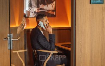 Zakelijke man telefoneert in modern ingerichte kantoorruimte op Coolsingel 139, Rotterdam Centrum. Huur deze stijlvolle werkplek voor comfortabele gesprekken en productieve momenten.