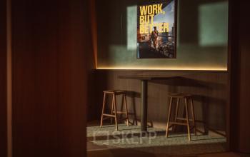 Gezellige zitplek met houten tafel en krukken, omringd door warme verlichting in een kantoorpand aan de Coolsingel 139, Rotterdam Centrum. Poster met inspirerende tekst aan de muur.