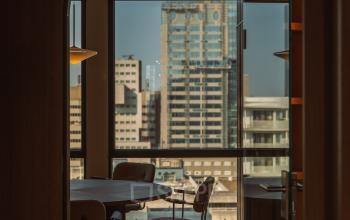 Lichte kantoorruimte met vergadertafel en stoelen, uitkijkend over de skyline van Rotterdam. Grote ramen bieden een prachtig uitzicht, ideaal om te huren op Coolsingel 139, Rotterdam Centrum.