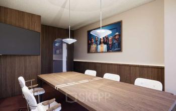 Moderne vergaderruimte in kantoorpand op Coolsingel 139, Rotterdam Centrum. Houten tafel met comfortabele stoelen, voorzien van moderne verlichting en kunst aan de wand. Ideaal voor bijeenkomsten, kantoorruimte huren in het hart van de stad.