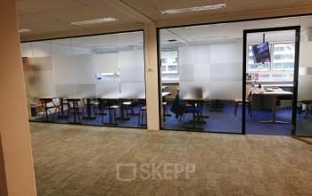 Kantoorruimte huren in Rotterdam Centrum aan Wijnhaven 76, met glazen wanden en blauwe vloerbedekking. Het kantoorpand is ruim en biedt een moderne omgeving voor werk en vergaderingen.