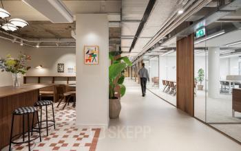 Modern kantoorpand op Stadhuisplein 9-23, Rotterdam Centrum met open werkruimtes en glazen wanden, ideaal voor kantoorruimte huren. Een persoon loopt langs bureaus in een lichte, strak ingerichte omgeving.