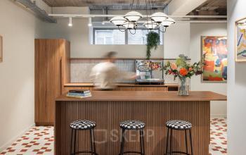 Gezellige pantry in een kantoorpand aan Stadhuisplein 9-23 in Rotterdam Centrum, met retro barkrukken en kleurrijke kunst, ideaal voor een informele pauze tijdens kantooruren.