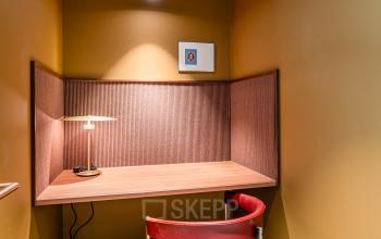 Kantoorruimte huren in Rotterdam Centrum op Stadhuisplein 9-23. Geisoleerde werkplek met een rode stoel en bureau, omgeven door warme okerkleurige muren. Ideaal voor geconcentreerd werken in het kantoorpand.