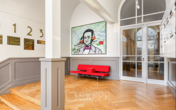 Entree van een kantoorpand met houten vloer, moderne kunst aan de muur en een rode bank. Ideaal om kantoorruimte te huren in Rotterdam Centrum, Veerhaven 7.