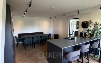 Moderne kantoorruimte in Rotterdam Centrum met houten vloer, stijlvolle bar met krukken en lange houten tafel met stoelen. Veel natuurlijk licht en groene planten voor frisse uitstraling.