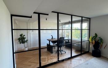 Moderne kantoorruimte met houten vloer en glazen wanden, uitgerust met een bureau en planten. Ideaal voor wie een kantoorpand wil huren in Rotterdam Centrum.