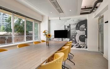Vergaderruimte in kantoorpand op Coolsingel 104, Rotterdam Centrum, met gele stoelen, lange tafel, muurdecoratie en groot raam met uitzicht.