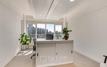 Ruime kantoorruimte met grote ramen en uitzicht op het stadscentrum van Rotterdam, gelegen aan de Coolsingel 104. Kantoor is voorzien van een bureau en enkele planten, ideaal voor inspirerend werken.