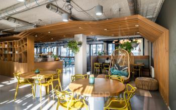 Moderne en lichte kantoorruimte met houten en gele accenten, ideaal voor informele bijeenkomsten en ontspannen werkmomenten op Westblaak 180 in Rotterdam Centrum. Planten en stijlvolle lampen geven de ruimte een frisse uitstraling.